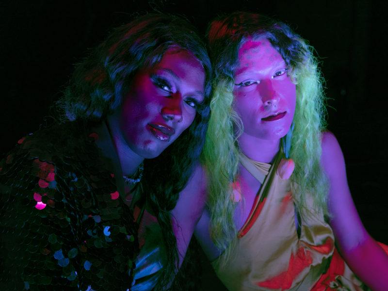 Jade Guanaro Kuriki-Olivo and Lexii Foxx sit close together, leaning on one another, both facing the camera.