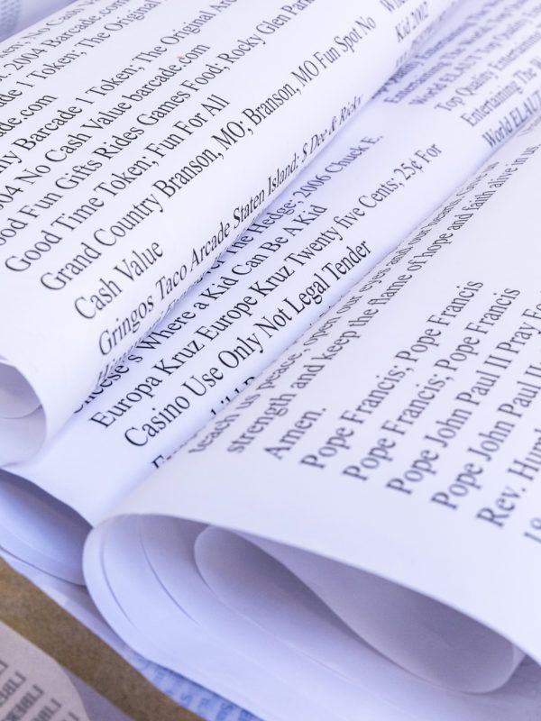 Folded papers with long lists of text are beside and atop one another within the image.