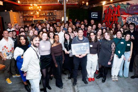 A large group of people posing together indoors, with one person holding a sign that says Art21.