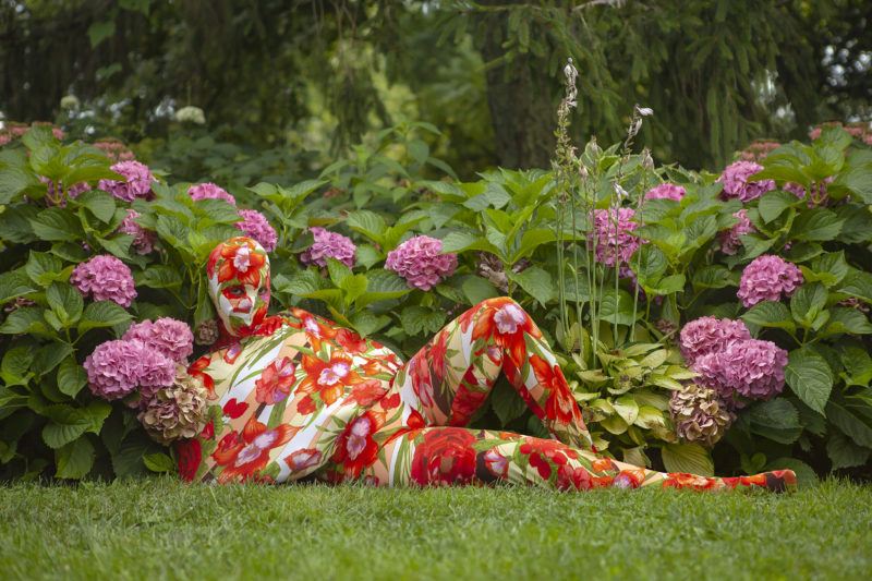 Person in a floral bodysuit blends in with a garden of pink hydrangeas, lying on the grass.