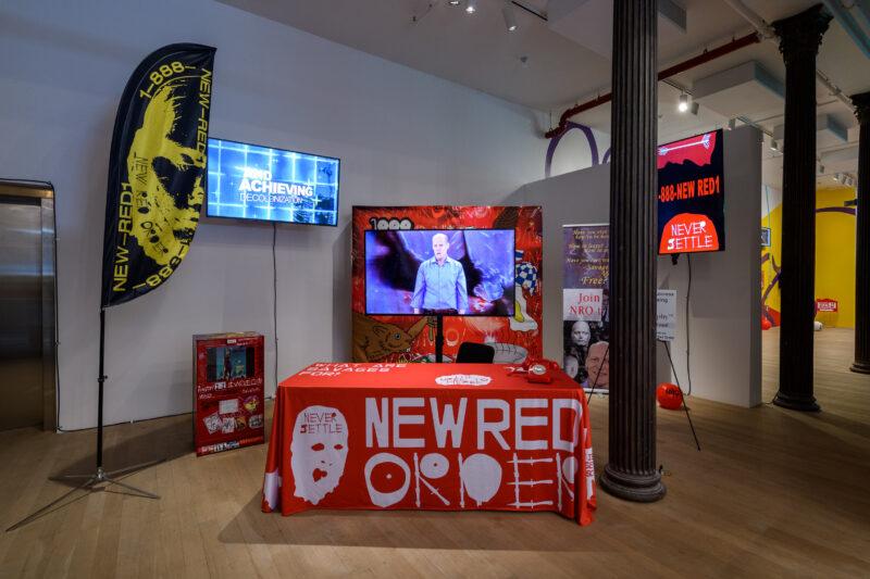 A promotional booth with "NEW RED ORDER" branding, display screens, banners, and informational materials set up in a modern indoor space.