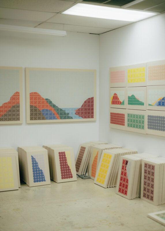 Stacks of colorful canvases on the floor underneath several canvases hanging on the walls.