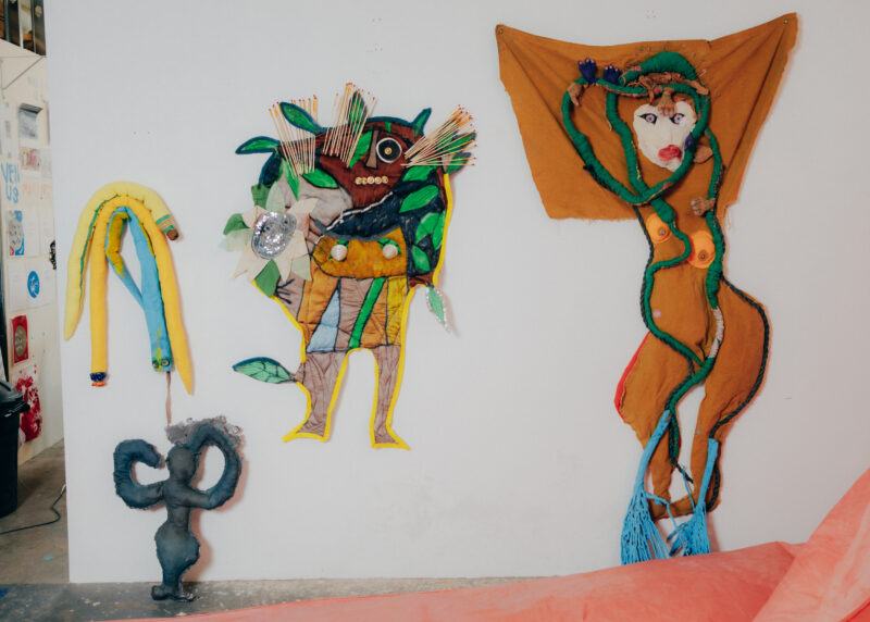 A white wall in the studio with fabric figures hanging on it.