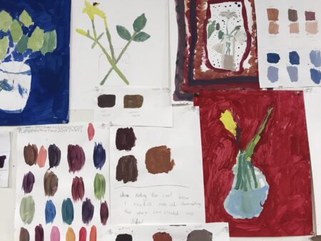 A collage of paintings and color swatches featuring vases with flowers and color tests pinned to a white wall.