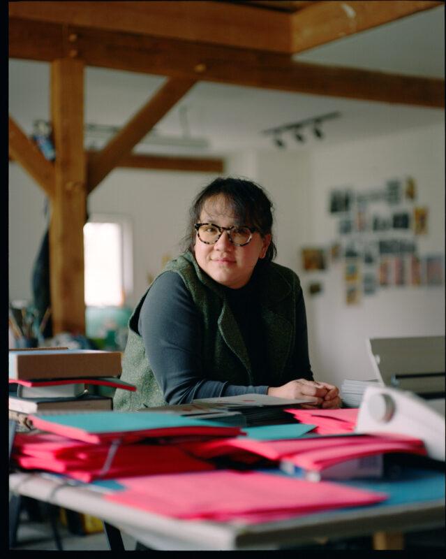 Tammy Nguyen leaning on a table covered in bright pink and blue papers.
