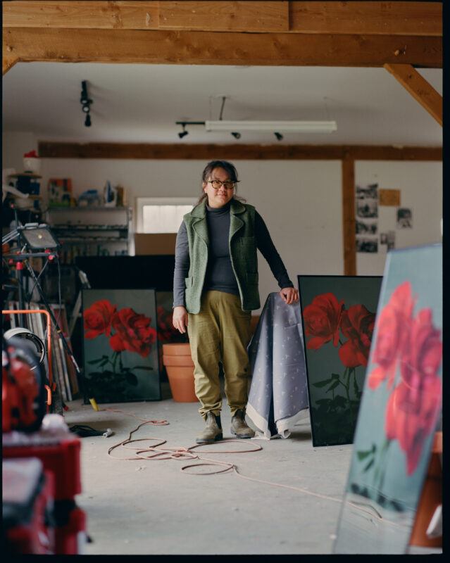 Tammy Nguyen standing in her studio surrounded by large framed paintings of roses.