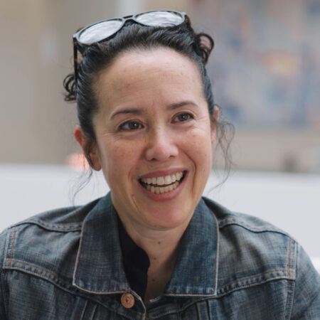 Sarah Sze with glasses pushed on top of her head, smiling looking out at the camera.